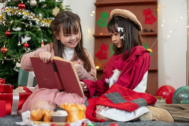 Due giovani ragazze asiatiche felici si divertono a leggere una favola di Natale in un libro