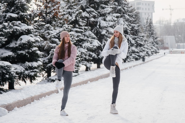 Due giovani ragazze atletiche fanno un riscaldamento prima di correre in una soleggiata giornata invernale. Uno stile di vita sano.