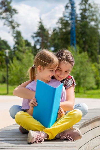 Due giovani ragazze seduti sulla panchina all'aperto leggendo un libro