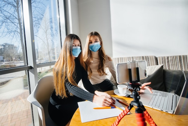 Due giovani ragazze siedono in un bar mascherate e conducono un video blog. Comunicazione alla telecamera.