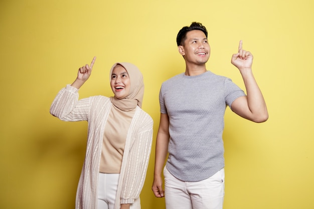 Due giovani, una donna hijab e un uomo con un'espressione felice hanno qualcosa di buono insieme isolato su sfondo giallo