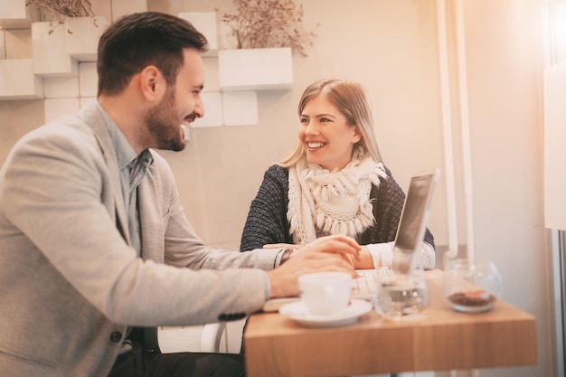 Due giovani uomini d'affari sorridenti che lavorano al computer portatile in una pausa al caffè. Messa a fuoco selettiva.