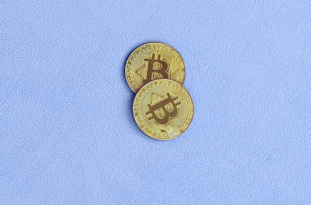 Due golden bitcoin giacciono su una coperta fatta di morbido e soffice tessuto in pile blu chiaro.