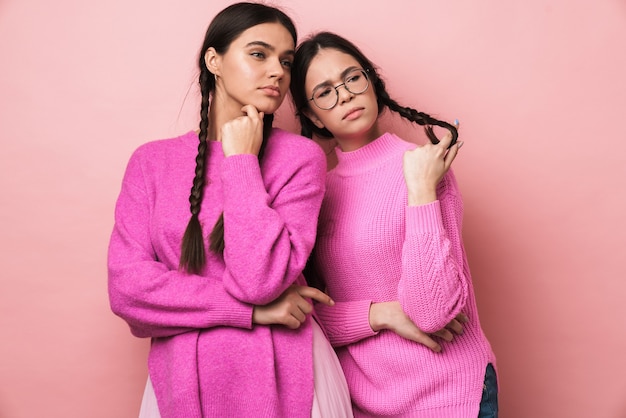 due gravi ragazze adolescenti con le trecce che guardano da parte il copyspace isolato su un muro rosa