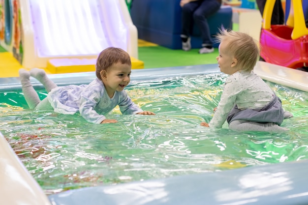 Due graziose bambine si siedono e ridono si divertono nella piscina dei giocattoli in un parco giochi per bambini