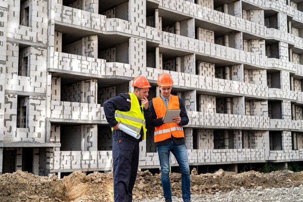 Due importanti lavoratori in tuta e casco guardano il tablet nel nuovo edificio. Concetto di costruzione