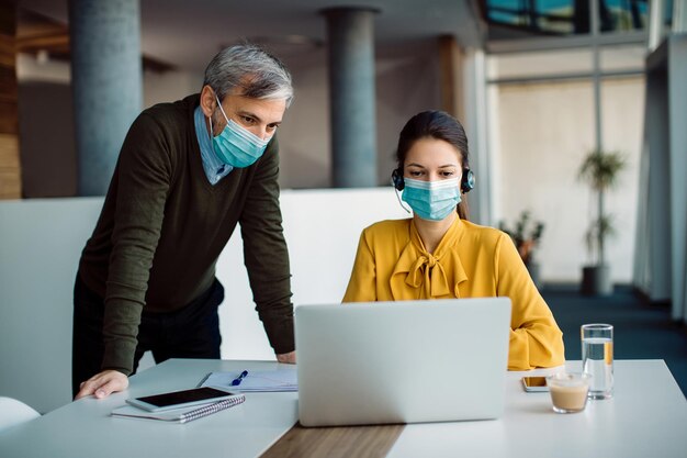 Due imprenditori con maschere facciali che lavorano su un computer in ufficio