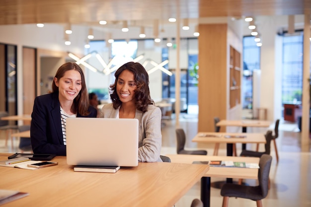 Due imprenditrici con laptop alla scrivania in ufficio open space che collaborano insieme al progetto