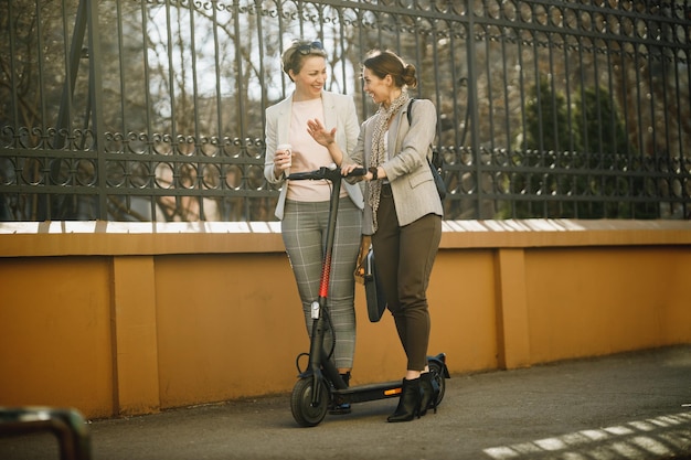 Due imprenditrici con uno scooter elettrico che vanno al lavoro e chiacchierano passeggiando per la città.