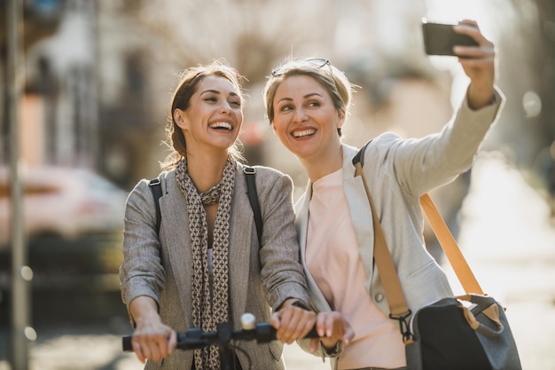 Due imprenditrici di successo che si fanno un selfie con lo smartphone mentre camminano per la città.