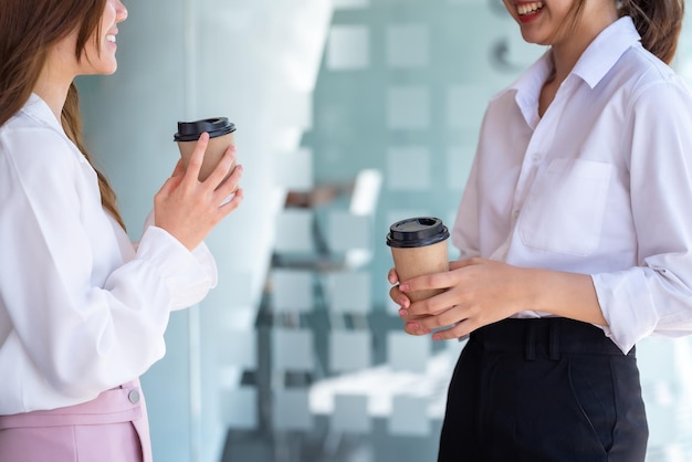 Due imprenditrici in piedi e parlando tenendo il caffè in ufficio