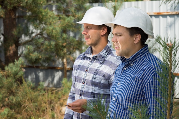 Due ingegneri con espressioni serie in piedi insieme in un cantiere a guardare qualcosa a sinistra del telaio