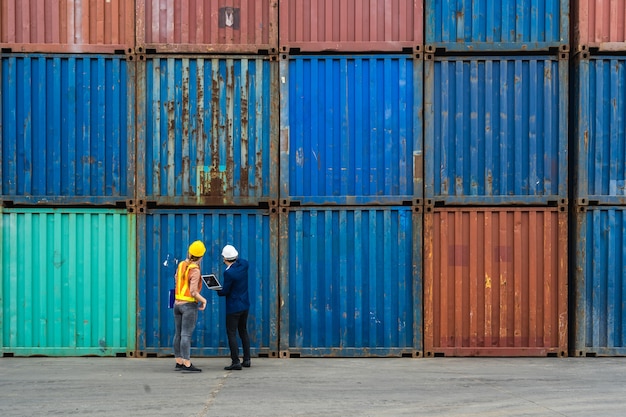 Due ingegneri tengono in mano un laptop, un documento per il controllo della qualità della scatola dei contenitori dalla nave da carico per l'esportazione e l'importazione, sfondo blu