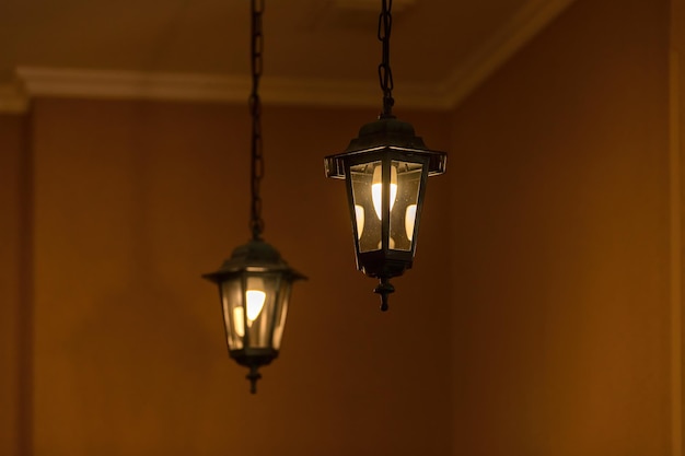 Due lanterne elettriche vintage sono appese a catene e si illuminano su uno sfondo arancione