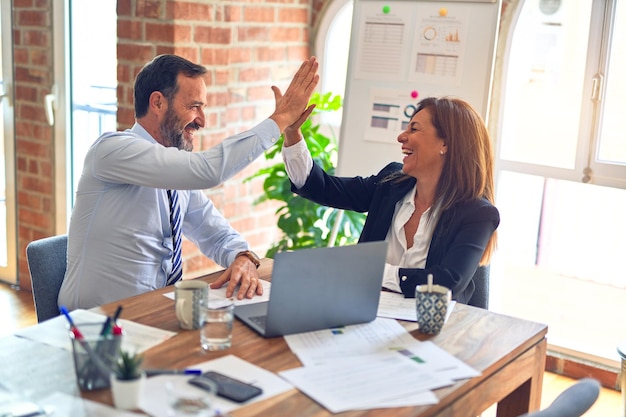 Due lavoratori d'affari di mezza età che sorridono felici e fiduciosi Lavorano insieme con il sorriso sulla mano del viso dando il cinque in ufficio