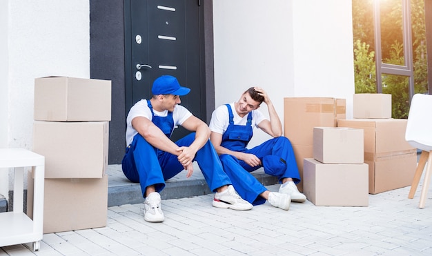 Due lavoratori dell'azienda di traslochi fanno una pausa seduti sul gradino