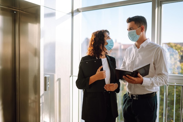 Due lavoratori in maschere protettive che discutono del progetto Lavoro in ufficio durante la quarantena