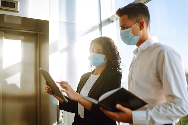 Due lavoratori in maschere protettive che discutono del progetto Lavoro in ufficio durante la quarantena