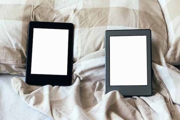Due libri elettronici moderni con schermi vuoti vuoti su un letto bianco e beige. compresse sulla biancheria da letto
