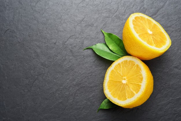 Due limoni tagliati a metà con foglie su sfondo nero ardesia