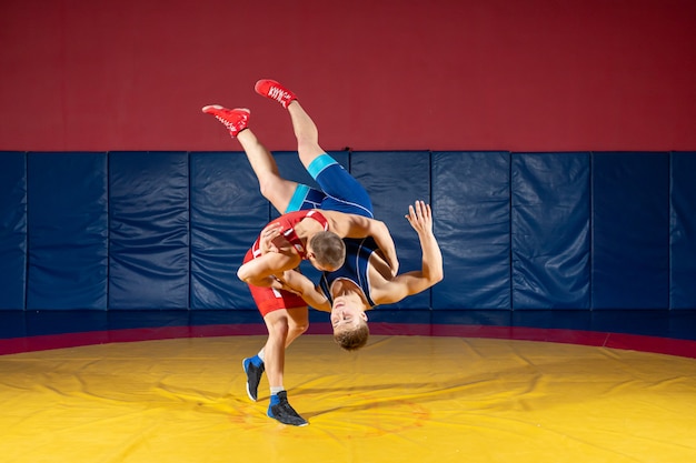 Due lottatori greco-romani in uniforme rossa e blu che lottano su un tappeto di wrestling giallo in palestra