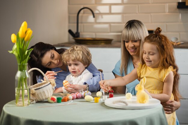 Due mamme con i loro bambini che colorano le uova di Pasqua mentre sono sedute in cucina