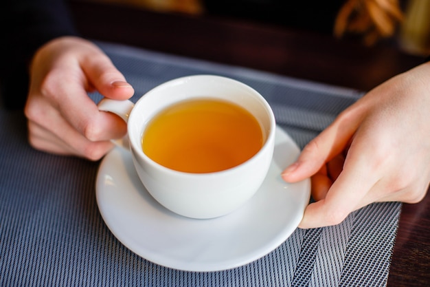 Due mani che tengono una tazza di porcellana all&#39;ora del tè nella caffetteria