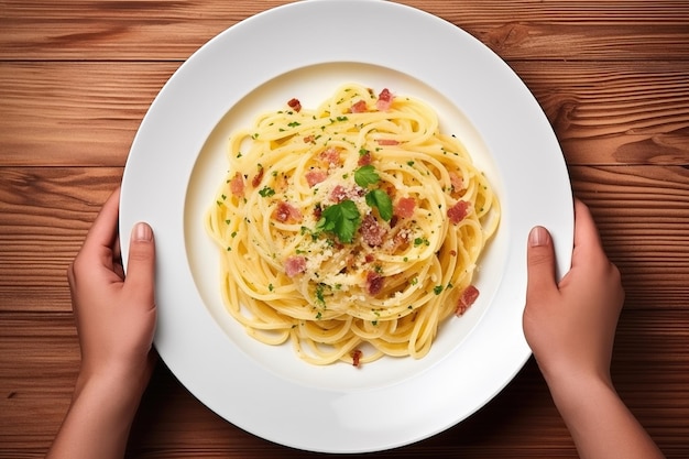 Due mani cullano delicatamente un piatto di Pasta Carbonara presentato su un tavolo di legno visto dall'alto