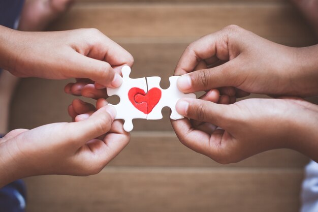 Due mani del bambino che collegano il pezzo del puzzle delle coppie con il cuore rosso tirato