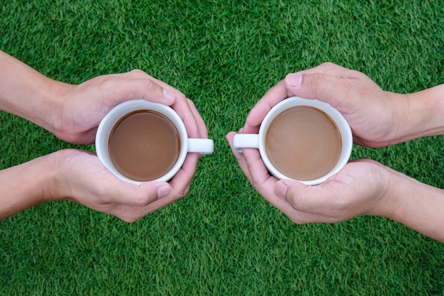 due mani e un paio di tazze di caffè su sfondo verde erba