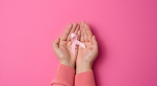 Due mani femminili tengono un nastro di seta rosa a forma di anello su sfondo rosa Simbolo della lotta contro il cancro al seno