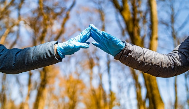 Due mani in guanti di lattice blu si toccano le dita l'una dell'altra Focolaio di quarantena Alberi nel parco