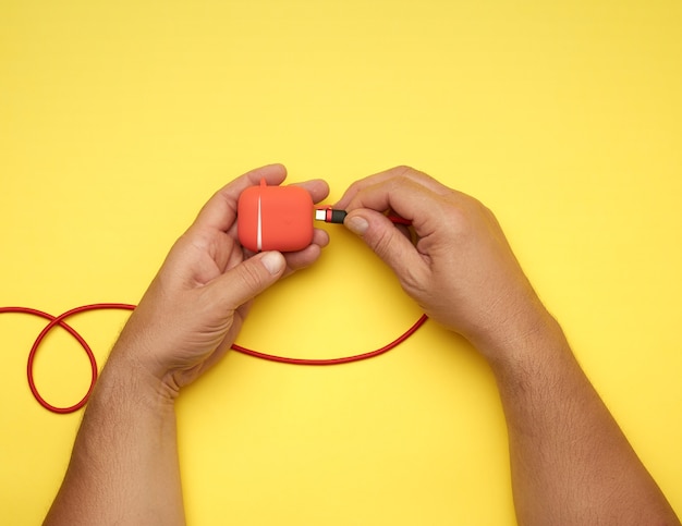 Due mani maschili stanno tenendo un cavo e una scatola rossa con cuffie wireless, tavolo giallo, vista dall'alto