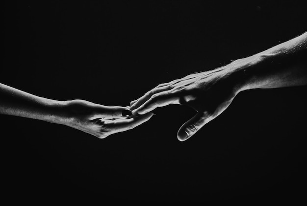 Due mani si allungano l'un l'altro sfondo nero coppia innamorata che tiene gli hads da vicino aiutando la mano supp