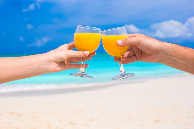 Due mani tengono i bicchieri con succo d'arancia in spiaggia