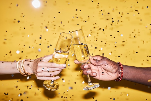 Due mani tintinnano bicchieri di champagne su sfondo giallo con coriandoli