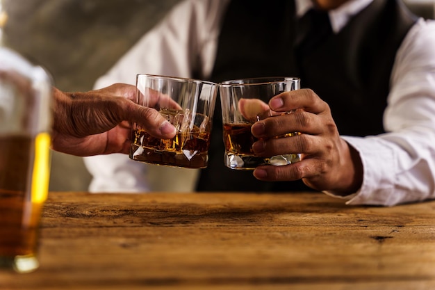 Due mani tintinnano bicchieri di whisky whisky sul divano Accogliente menu per bere al bar
