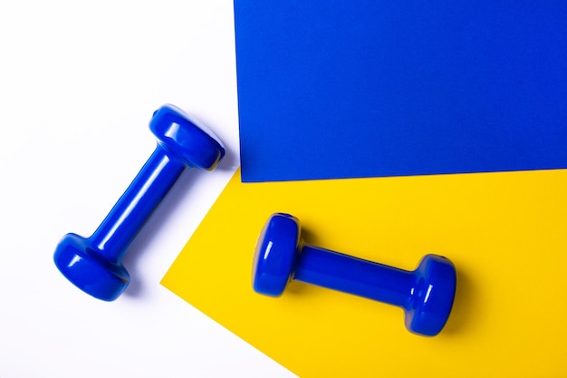 Due manubri fitness blu su sfondo bianco, giallo e blu. Attrezzatura per allenamenti ed esercizi a casa nella palestra flat lay. Manubrio sportivo per uno stile di vita sano vista dall'alto.