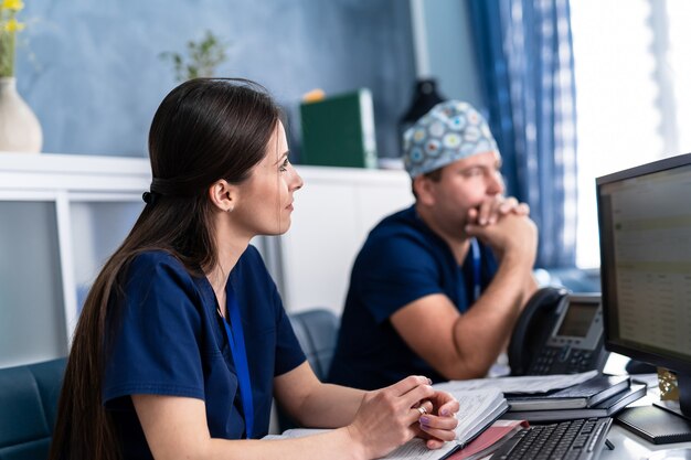 Due medici che discutono di competenze mediche in ufficio al computer. Medici uomo e donna.