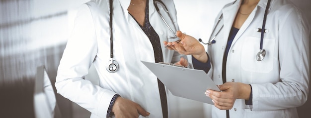 Due medici di sesso femminile stanno discutendo dei test medici del loro paziente, mentre si trovano in un ufficio clinico. I medici usano una lavagna per appunti al lavoro. Il lavoro di squadra in medicina.