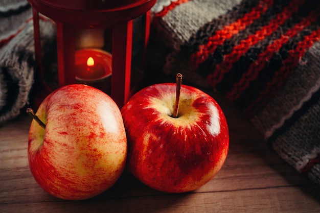 Due mele rosse, maglione di lana e una lanterna con una candela.