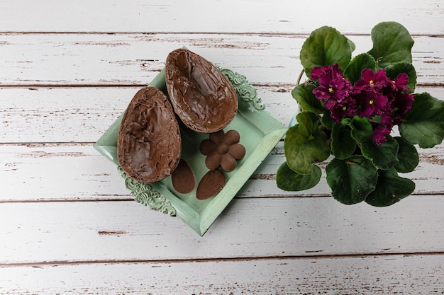 Due metà dell'uovo di Pasqua del cioccolato, su un piccolo vecchio vassoio. Accanto a mini cioccolatini e fiori.