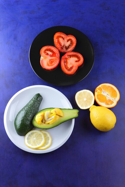 Due metà di un avocado maturo con seme su un piatto Primo piano di frutta verde e fette di agrumi e pomodoro su sfondo blu Concetto di cibo vegetariano