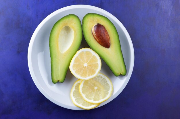Due metà di un avocado maturo con semi su un piatto bianco Primo piano frutta sana verde con agrumi su sfondo blu