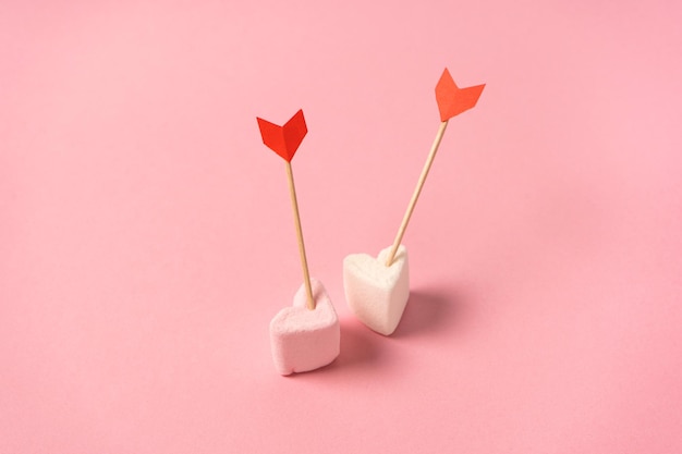 Due mini marshmallow rosa a forma di cuore su sfondo rosa con frecce d'amore. Concetto di amanti. Buon San Valentino