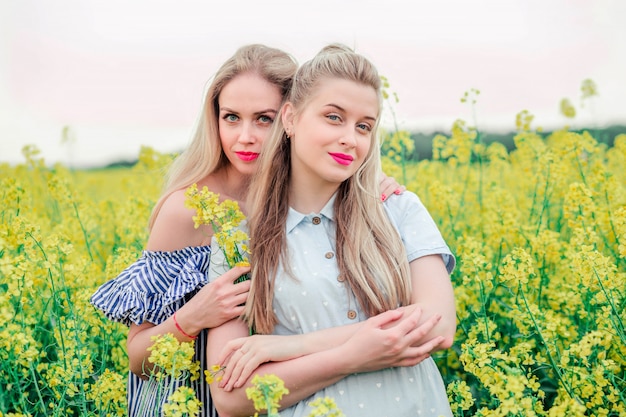 Due modelli di ragazze che posano insieme sulla macchina fotografica nel campo di colza