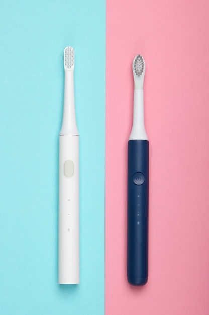 Due moderni spazzolini da denti elettrici sulla superficie pastello rosa blu
