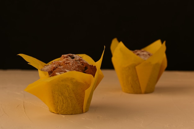 Due muffin con uvetta in una carta da pasticcere gelatina per cottura stand in diagonale su un tavolo bianco