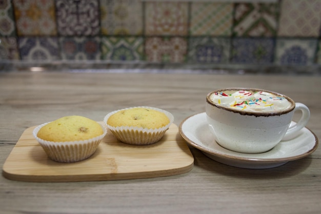 Due muffin con uvetta su un vassoio di legno e una tazza di cioccolata calda