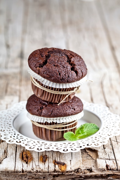 Due muffin freschi del cioccolato fondente con le foglie di menta sul piatto bianco.